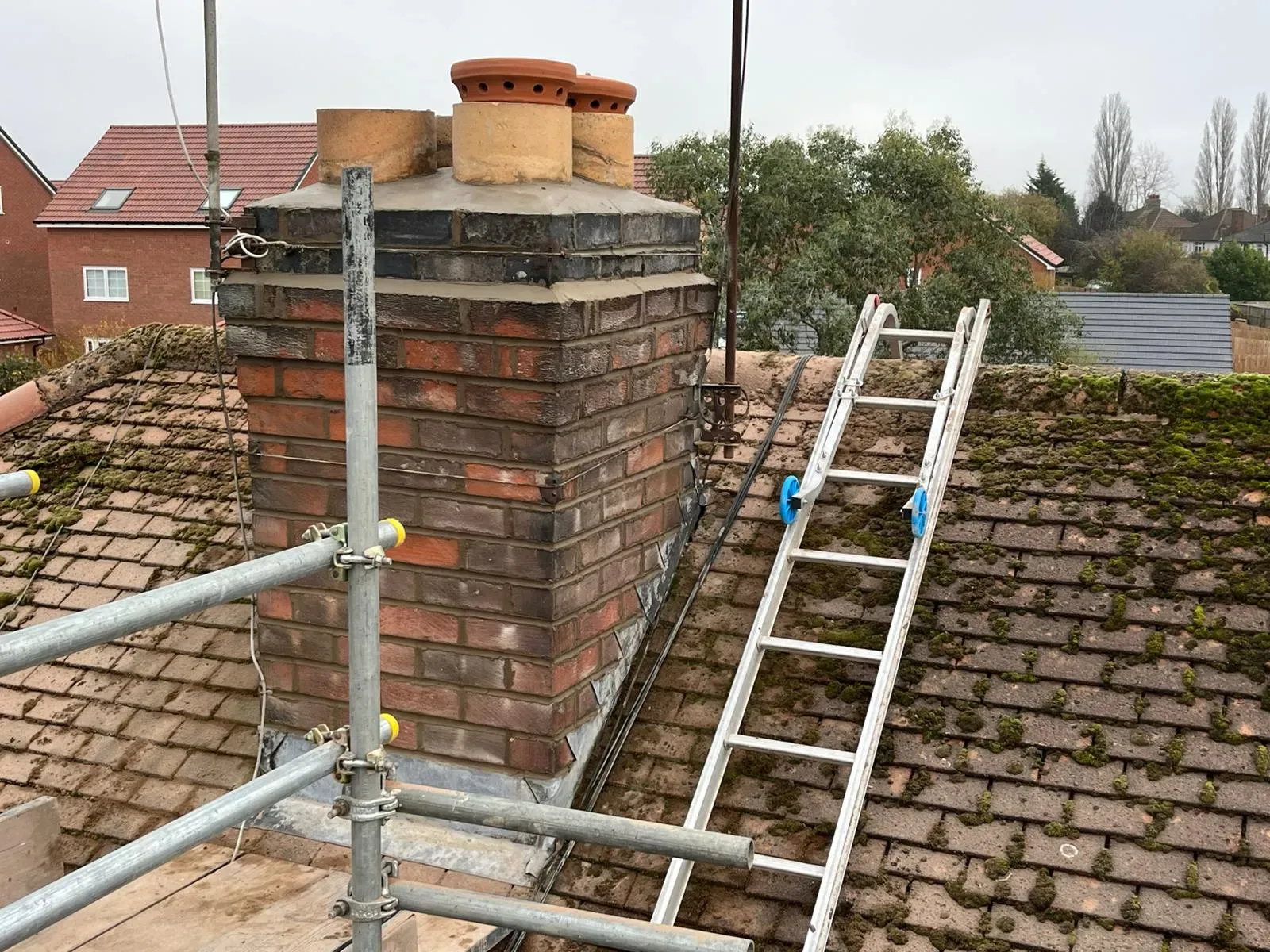 Chimney repairs and maintenance on a residential roof in Gloucestershire with scaffolding and roof ladder