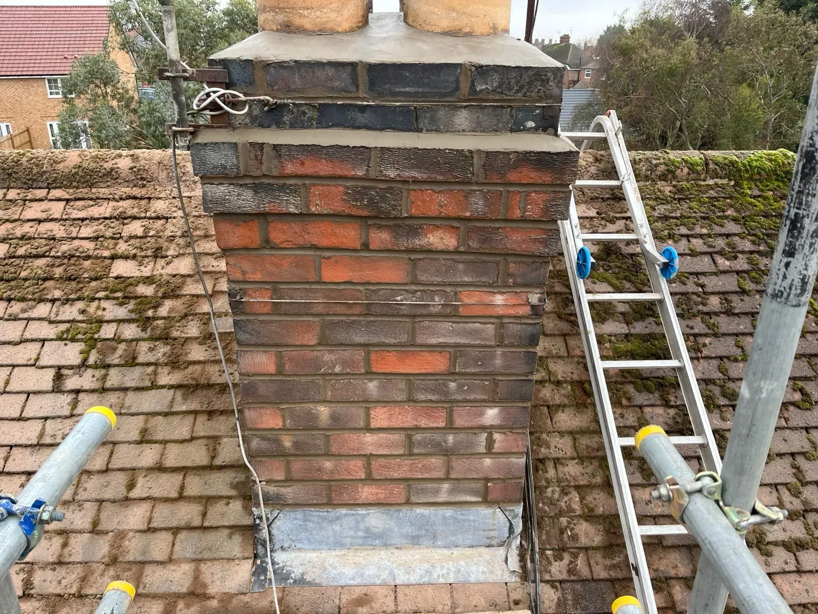 A brick chimney stack on a residential roof being repaired with fresh repointing and lead flashing work.